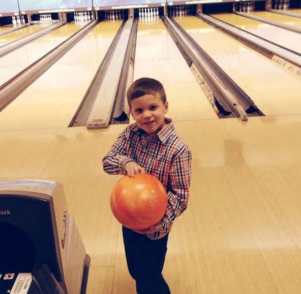 A young boy holding an orange bowling ball at Southland Bowling Lanes